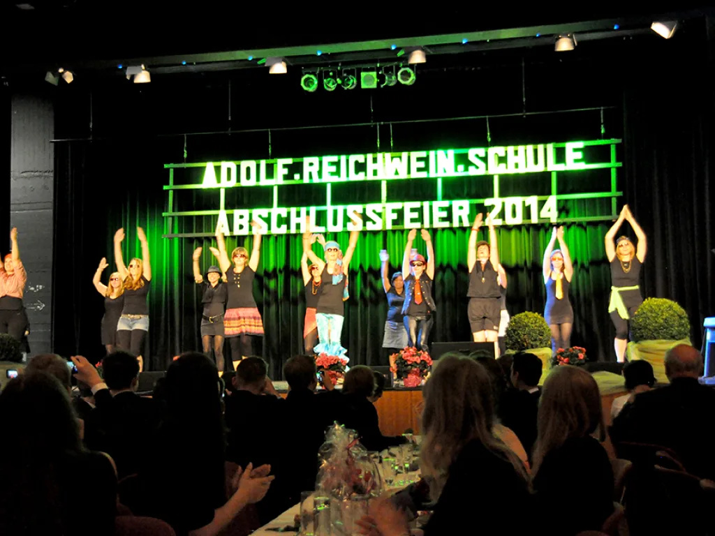 Tanzgruppe tritt vor grün beleuchteter Schriftwand auf.